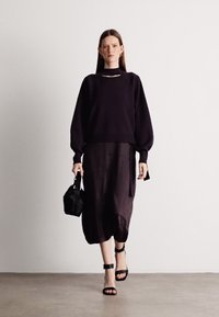 Tamno ljubičasti pulover s širokim izrezom, uparen s lepršavom tamno ljubičastom suknjom. Nosite ga s crnim sandalama na remen i malom torbicom.