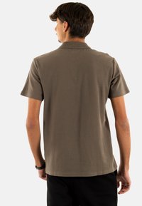 Polo de manga corta en color topo, con una tela texturada, cuello de canalé y dobladillo recto. La vista posterior muestra un corte relajado.