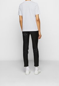 Bílé bavlněné tričko s krátkým rukávem, v kombinaci s černými slim-fit kalhotami. Oblečení doplňují bílé tenisky.