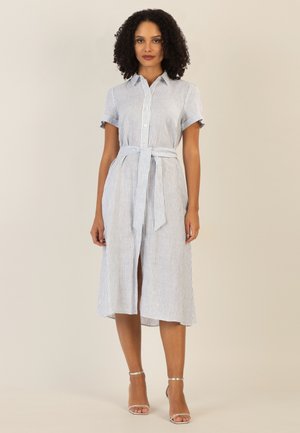 Woman with curly hair wearing a white and blue vertical striped midi shirt dress with a waist tie and silver ankle-strap heels.