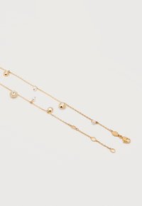 Δύο λεπτά βραχιόλια από χρυσή αλυσίδα με μικρές λευκές πέρλες και διάφανα κρυσταλλικά γοητευτικά στοιχεία σε απλό λευκό φόντο.