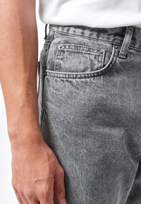 Jeans in denim grigio con una vestibilità classica, dotati di tasca frontale, dettagli in metallo e un tessuto leggermente strutturato.