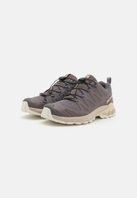 Grå mesh sportskor med en texturerad yta, elastiska snören och en slitstark gummisula. Har en kontrasterande beige mellansula.