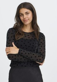 Sort langærmet top med et gennemsigtigt design, som har velour hjerte mønstre. Strukturert overflade med rund halsudskæring og tætsiddende manchetter.