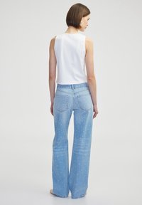 Lichtblauwe uitlopende jeans met witte studded versieringen, gecombineerd met een aansluitend wit mouwloos topje, dat een gladde textuur en een casual ontwerp laat zien.