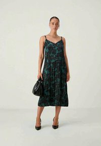 Midi haljina bez rukava u tamno tirkiznoj boji s crnim cvjetnim uzorcima, izrađena od laganog materijala i opuštenog kroja, uparena s malom crnom torbicom.