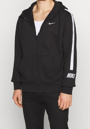 Schwarze Zip-Hoodie aus Baumwollmischung. Mit einer Kapuze mit Kordelzug, zwei Fronttaschen und weißem Nike-Branding auf den Ärmeln.