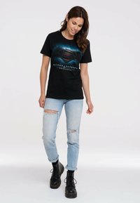 Black T-shirt with a colorful Batman vs. Superman graphic. Paired with light blue distressed jeans and black lace-up boots.