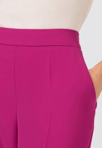 Fuksia-housut, joissa on sileä pinta, korkea vyötärö ja sivutaskut. Kankaan on näkyvästi kevyt ja se laskeutuu kauniisti.