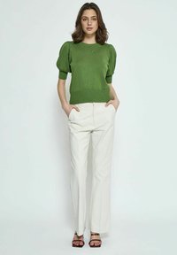 Maglione verde a maglia con maniche a sbuffo corte, abbinato a pantaloni larghi color crema. Sandali con una sottile fascia completano l'outfit.