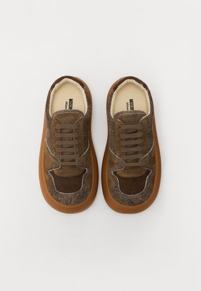 Adidași din suede maro cu talpă din cauciuc bej, accente gri și sfori maro. Prezintă secțiuni decupate pe laturi și o suprafață texturată.