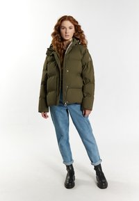 Oliven grøn pufferjakke med hætte, lynlås og sølv hardware. Kombineret med lyseblå jeans og sorte klodsede støvler.