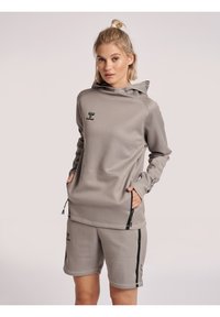 Felpa atletica grigia con tasca a marsupio e zip, abbinata a pantaloni corti coordinati. Presenta dettagli con logo e un tessuto morbido e texture.