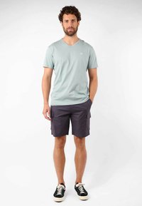 T-shirt vert clair à col en V, shorts cargo gris foncé avec poches latérales, baskets noires à semelles blanches, portés de manière décontractée.