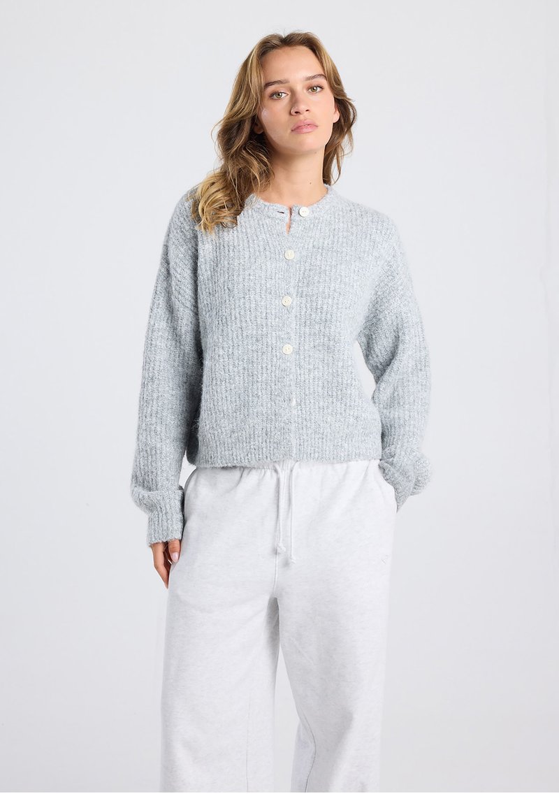 Gray knitted cardigan with a ribbed texture, featuring a round neckline, five buttons, and dropped shoulders, paired with light gray sweatpants.