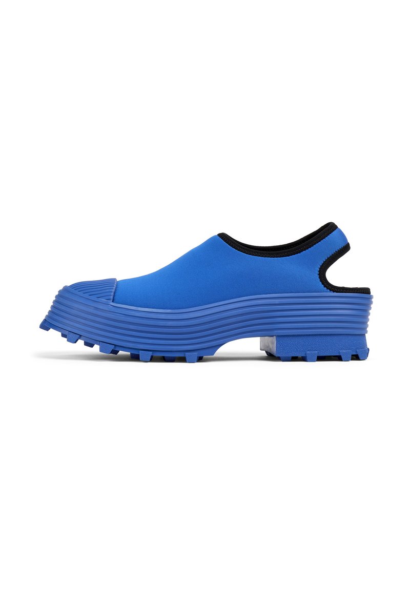 Blå slip-on skor med en tjock ruggad sula, rundad front och en svart trimmad öppning för enkel påtagning. Tillverkade av mjukt, flexibelt material.
