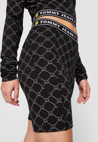 Pantaloni corti neri con un motivo ripetuto di faccine sorridenti bianche, dotati di una vita elastica con marchio. Realizzati in tessuto elasticizzato, dalla consistenza liscia.