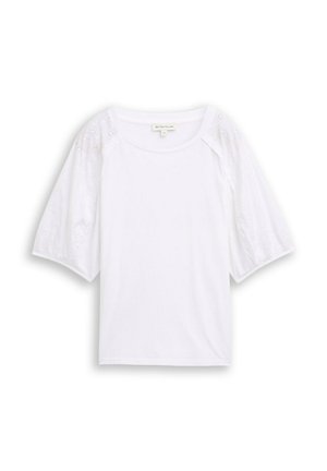 Blouse blanche avec un col rond et des manches courtes bouffantes présentant une broderie florale ajourée.