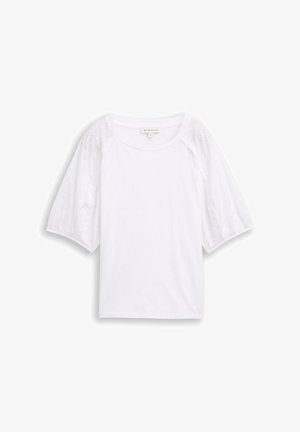 Blouse blanche avec un col rond et des manches courtes bouffantes présentant une broderie florale ajourée.