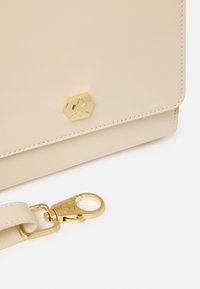 Borsa a tracolla in pelle beige con chiusura a calamita a forma di esagono e hardware dorato, dotata di tracolla removibile e dettagli di cucitura visibili.