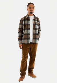 Brun och grå rutig flanellskjorta med knappar, vit t-shirt under, bruna korduroybyxor och bruna sneakers.