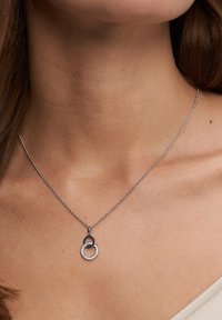 Sølvkæde med sammenkædede cirkulære vedhæng; det ene prydet med klare rhinsten, det andet med en glat metaloverflade.