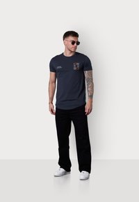 T-shirt en coton bleu marine à manches courtes, col rond et impression graphique sur la poitrine. Associé à un pantalon noir et des baskets blanches.