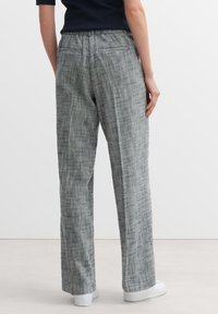 Grijze gebreide broeken met een relaxed fit, voorzien van een trekkoord in de taille en twee achterzakken, gedragen met witte sneakers.