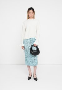 Weißer gestrickter Pullover, hellblauer Paillettenrock, schwarze Handtasche und schwarze spitze Schuhe auf einem schlichten weißen Hintergrund.