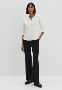 Top bianco a trama con scollatura a V e maniche a tre quarti, abbinato a pantaloni neri a zampa e scarpe nere senza lacci.