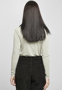 Světle zelené tričko s dlouhým rukávem a přiléhavými rukávy, kombinované s černými manšestrovými kalhotami s vysokým pasem. Pohled zezadu ukazuje hladkou texturu a střihané linie.