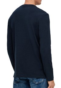 Granatowa koszula z długim rękawem z okrągłym dekoltem o gładkiej strukturze, zestawiona z niebieskimi dżinsami. Czysty design bez widocznych wzorów czy logo.