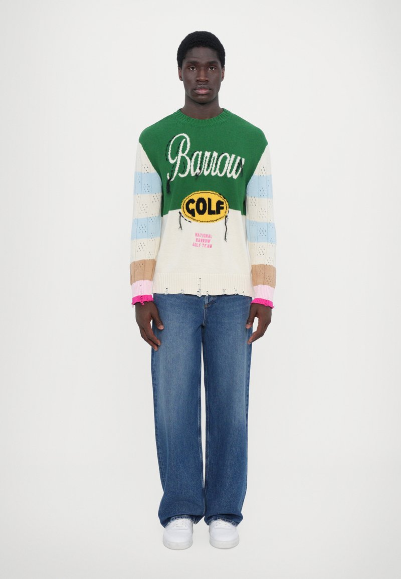 Farverig strikket sweater med grønne, blå og cremefarvede striber, prydet med "Barrow GOLF" logo, kombineret med vide blå jeans og hvide sneakers.
