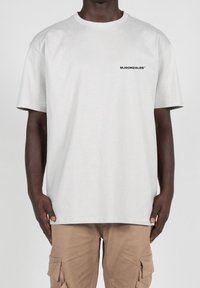 Lys grå bomulds T-shirt med korte ærmer og rund hals, med et lille sort logo trykt på venstre bryst.