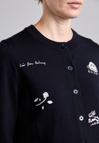 Cardigan navy con design floreali e animali ricamati, colletto rotondo e bottoni blu. Tessuto morbido con una texture liscia.