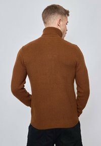Pull en maille côtelée marron avec un col montant, des manches longues et un tricot texturé. Fabriqué à partir d'un matériau doux, conçu pour un ajustement confortable.