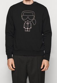 Sudadera negra con un gráfico de un personaje de dibujos animados con gafas de sol y traje, contorneado en multicolor, de material suave y con cuello redondo.