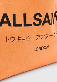 Orange textilväska med djärv svart "ALLSAINTS"-logotyp och ytterligare text på japanska, med en slät texturerad yta.