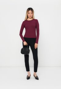 Top long à manches longues bordeaux côtelé associé à un pantalon noir ajusté et un sac à main noir texturé. Les chaussures sont pointues avec un détail de lanière.