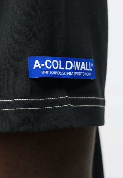 Čierne bavlnené tričko s modrou nášivkou s nápisom "A-COLD.WALL* BRITISHINDUSTRIASPORTSWEAR" a bielym prešívaním pozdĺž lemovania.