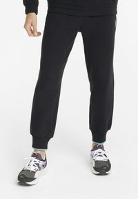 Sorte joggebukser med ribbede mansjetter, med et logo-merke, sammen med sorte og lilla joggesko med hvite snøringer og polstrede såler.