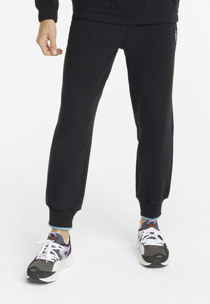 Sorte joggebukser med ribbede mansjetter, med et logo-merke, sammen med sorte og lilla joggesko med hvite snøringer og polstrede såler.