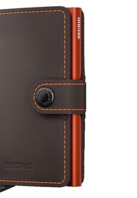 Brown leather wallet with orange stitching, featuring a black snap button and a red aluminum cardholder embedded on the side.
