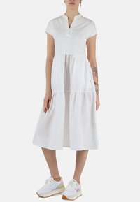 Abito bianco a maniche corte con colletto a scollo a V, design a strati e una gonna fluida. Abbinato a sneakers colorate con dettagli bianchi e pastello.