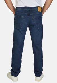Vaqueros de mezclilla azul oscuro con corte recto, que presentan dos bolsillos traseros y una etiqueta de cuero marrón en la cintura. Llevados con zapatillas blancas.