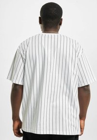 T-shirt blanc à manches courtes avec des rayures verticales noires, présentant une coupe décontractée et un col rond. Tissu lisse et léger.