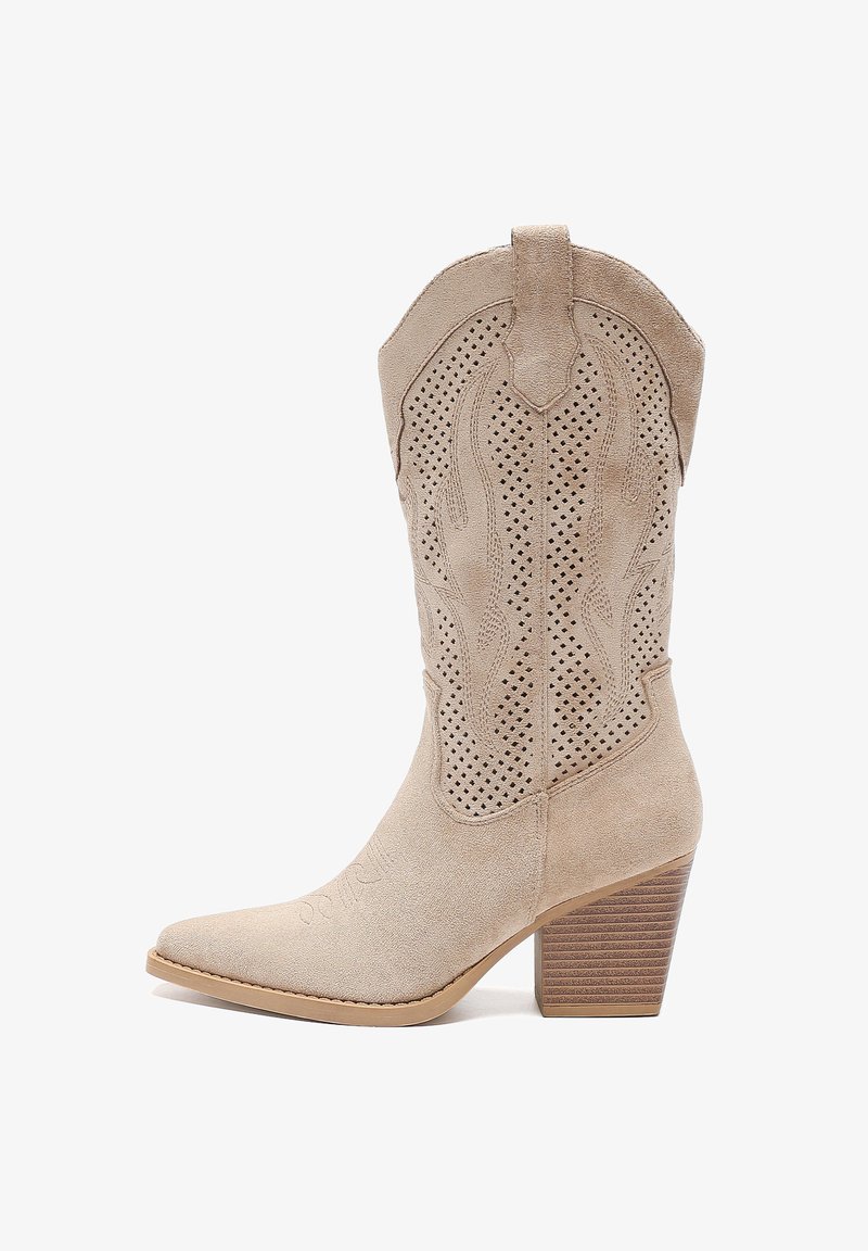 Bota de vaquero de ante beige con detalles perforados, puntera puntiaguda y tacón de madera apilada. Presenta costuras decorativas en el eje.