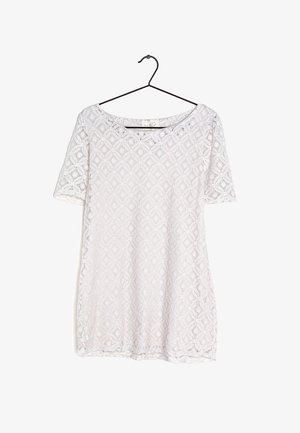 Bílé krátké krajkové šaty s květinovým diamantovým vzorem zavěšené na černém ramínku na bílém pozadí.