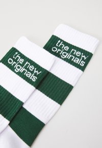 Fehér, térd fölé érő zoknik zöld vízszintes csíkokkal és a "the new originals" felirattal. Bordás anyagból készült, puha tapintással.