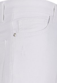 Valged denim püksid, millel on tagatasku detail, vöökoht on ümber õmmeldud ja tasku lähedal on hõbedane riistvara aksent.